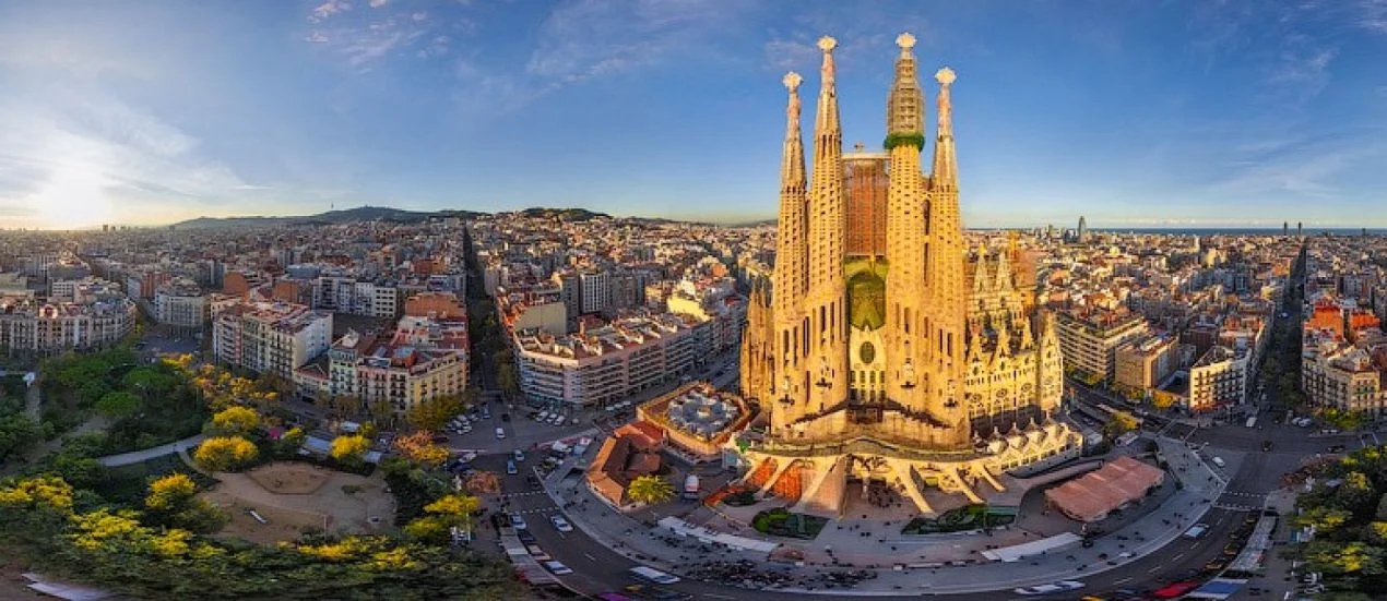Park Güell'deki renkli mozaiklerle süslenmiş bir bankta oturan insanların şehir manzarasını izlemesi